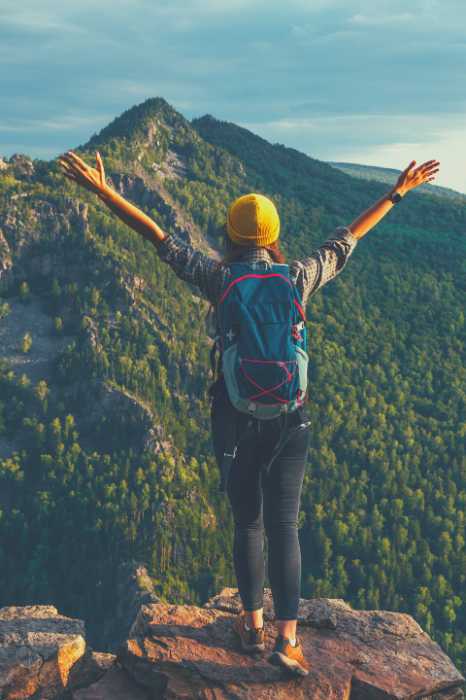 A woman stands on top of a cliff with her arms outstretched overlooking a beautiful mountain.  She has experienced the benefits of life coaching.